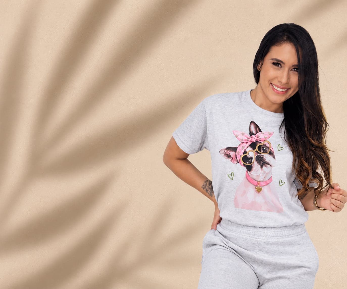 Modelo sonriendo con camiseta gris estampada con un bulldog francés con moño rosado y gafas de corazón
